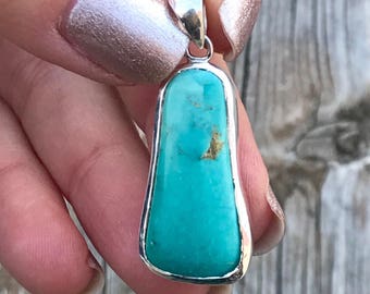 May include: A turquoise gemstone pendant set in sterling silver. The pendant is shaped like a teardrop and has a smooth, polished finish.