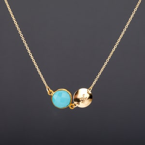 Puede incluir: Un collar de cadena dorada con una piedra preciosa azul turquesa y un colgante de disco dorado con un pequeño diseño.