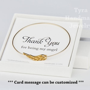 May include: A white box with a gold bangle bracelet with a gold angel wing charm. The box has a card inside that says "Thank you for being my angel." The card is customizable.