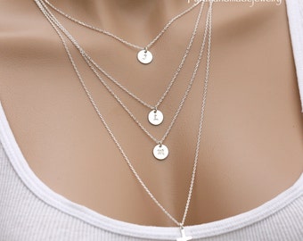 May include: A silver necklace with four pendants. The pendants are round and have the letters J, L, and M engraved on them. The bottom pendant is a cross.