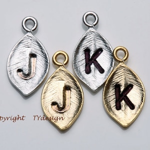 May include: Three leaf-shaped charms with initial letters J and K. The charms are made of silver, gold, and gold with a burgundy letter. The charms have a textured surface.