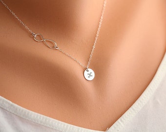 Puede incluir: Un collar de plata con un dije de símbolo de infinito y un pequeño dije redondo con una inicial "K" grabada.