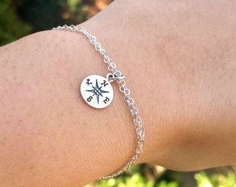 May include: A silver chain bracelet with a compass charm. The compass charm has a silver star in the centre and the letters N, S, E, and W around the edge.