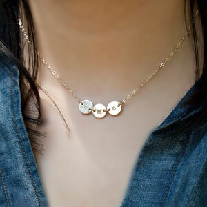 May include: A gold chain necklace with three round pendants, each with a letter engraved on it. The letters are K, W, and O.