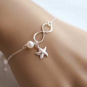 Puede incluir: Pulsera de plata de infinito con un encanto de perla y una estrella de mar. La pulsera está en la muñeca de una modelo.