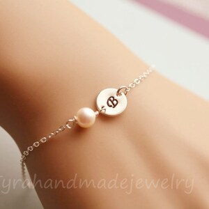 May include: A silver chain bracelet with a single pearl charm and a silver disc charm with the letter "B" engraved on it.
