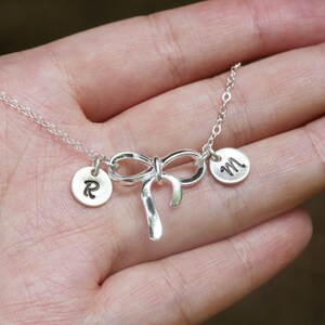 May include: Silver necklace with a bow charm and two personalized discs with the letters 'R' and 'M'.