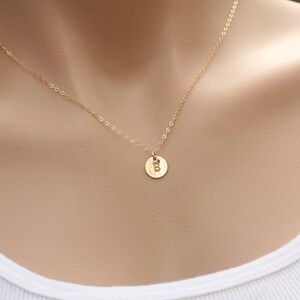 May include: A gold chain necklace with a small gold disc pendant featuring the letter "B" engraved on it.