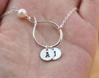Puede incluir: Collar de infinito de plata con un dije de perla y dos pequeños dijes redondos con las letras A y J.