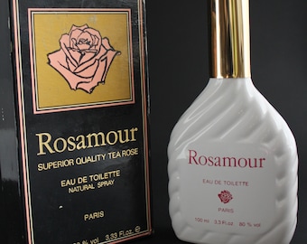 May include: A white Rosamour Eau de Toilette perfume bottle with a gold cap and a matching box. The box is black with gold and pink accents, featuring a rose illustration and the text "Rosamour". The bottle contains 100 ml.