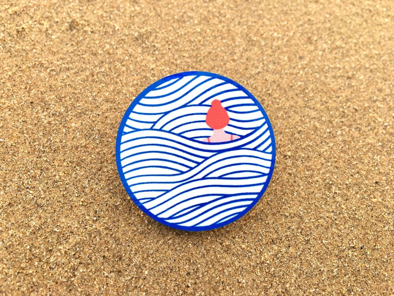 May include: A round sticker featuring a blue and white wave pattern. A red figure is partially submerged in the waves.