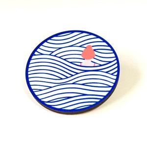 May include: A round wooden pin featuring a blue and white wave pattern. A small pink figure is partially submerged in the waves.