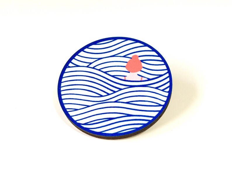 May include: A round wooden pin featuring a blue and white wave pattern. A small pink figure is partially submerged in the waves.