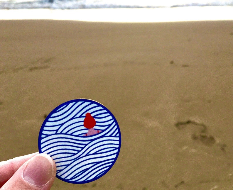 May include: A blue and white sticker with a stylised illustration of a person with red hair swimming in waves.