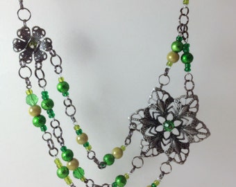 May include: A silver chain necklace with green and gold beads and two silver flower charms.