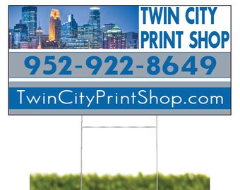 May include: A blue and white sign with the text "Twin City Print Shop" and the phone number "952-922-8649". The sign also includes the website "TwinCityPrintShop.com". The sign is in front of a blurred image of a city skyline.