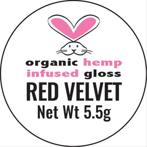 May include: A white circle with a black outline features a pink heart-shaped bunny head with the text "organic hemp infused gloss RED VELVET Net Wt 5.5g"