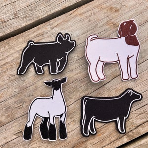 May include: Four embroidered patches of farm animals: a black pig, a white and brown goat, a black and white lamb, and a black cow. Each patch has a white outline and is set against a weathered wood background.