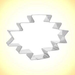 May include: A silver-colored metal cookie cutter in a geometric design. The cutter has a zig-zag pattern around the edges, forming a shape with a central open space. The cutter is designed for baking and crafting.