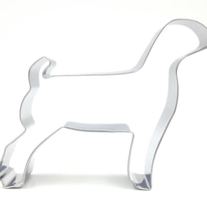 May include: A shiny, silver-colored metal cookie cutter in the shape of a dog. The dog is standing, with its tail curled up. The cookie cutter is on a white background.