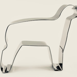 May include: A stainless steel alpaca-shaped cookie cutter. The cutter is a single piece of metal, with a detailed outline of an alpaca. The alpaca is standing, with its head held high. The cutter is designed for baking.