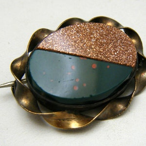 Puede incluir: Un broche vintage con un camafeo verde y cobre engastado en un marco de lat&oacute;n retorcido.