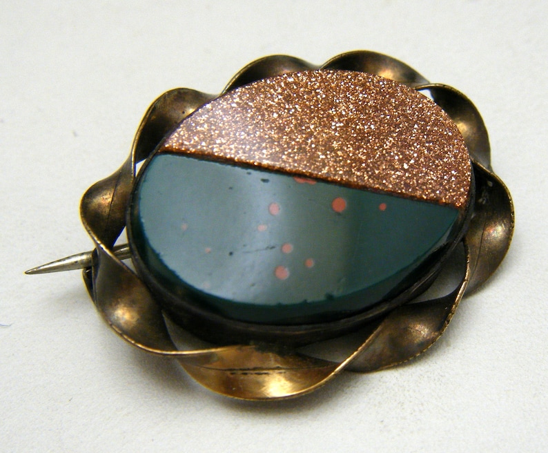 Puede incluir: Un broche vintage con un camafeo verde y cobre engastado en un marco de lat&oacute;n retorcido.