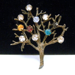 May include: A gold-toned tree brooch with colorful rhinestones. The tree has a thick trunk and many branches with clear, red, orange, blue, and black rhinestones.