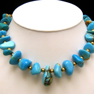 Op de afbeelding: Een turquoise en gouden ketting met een traanvormige hanger. De ketting is gemaakt van onregelmatig gevormde turquoise stenen en gouden kralen.