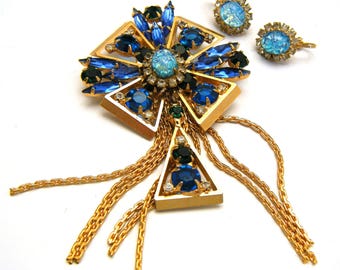 May include: A gold tone brooch with blue, green, and clear rhinestones. The brooch has a dangling chain with multiple strands. A matching pair of earrings with blue and clear rhinestones.