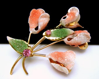 Puede incluir: Un broche de tono dorado con un grupo de cinco flores rosas y blancas con hojas verdes y diamantes de imitación rosas.