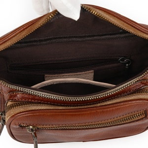 May include: A brown leather fanny pack with a zippered main compartment and a smaller zippered pocket inside. The bag has a brown canvas lining and a gold zipper.