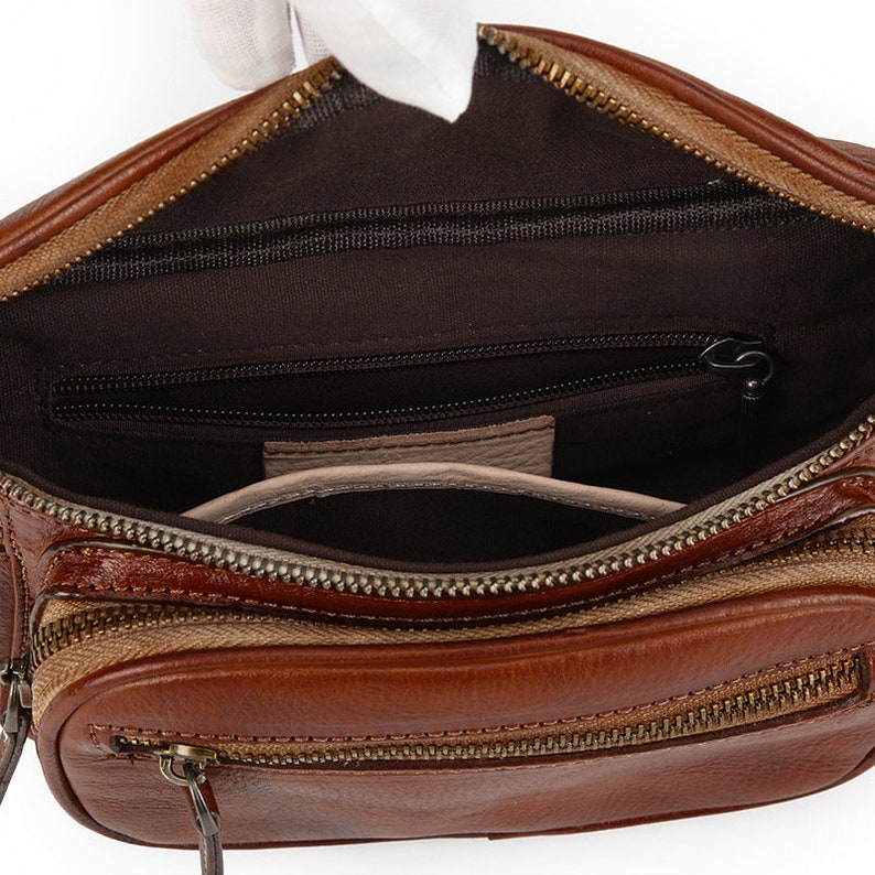 May include: A brown leather fanny pack with a zippered main compartment and a smaller zippered pocket inside. The bag has a brown canvas lining and a gold zipper.