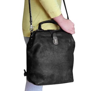 May include: Black leather satchel bag with a top handle and a shoulder strap. The bag has a rectangular shape with a metal clasp closure. The leather has a distressed appearance.