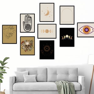 May include: A collection of framed art prints featuring celestial and mystical themes. The prints include images of a hand with intricate designs, phases of the moon, an eye, a skull with flowers, and a sun with hands. The frames are black, and the backgrounds vary in color.