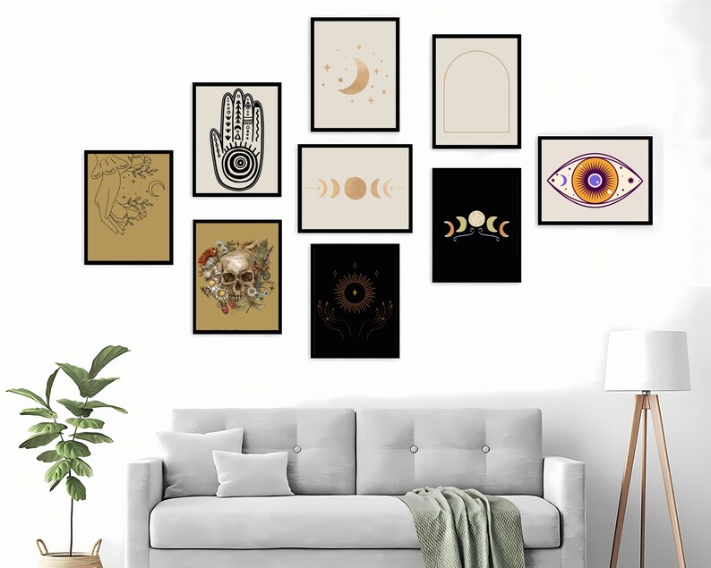 May include: A collection of framed art prints featuring celestial and mystical themes. The prints include images of a hand with intricate designs, phases of the moon, an eye, a skull with flowers, and a sun with hands. The frames are black, and the backgrounds vary in color.