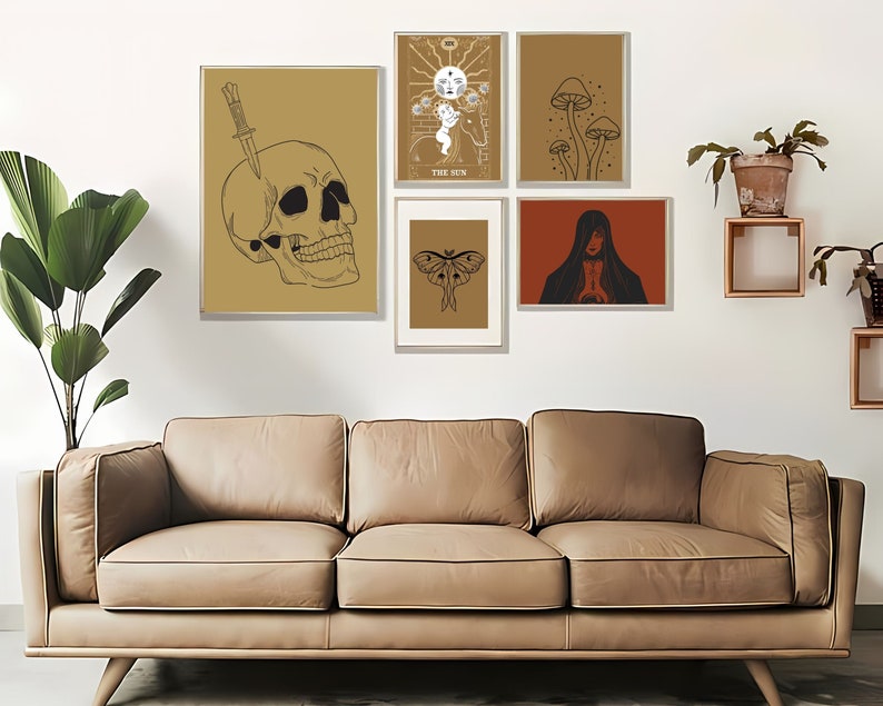 May include: A collection of framed art prints featuring mystical and gothic themes. The prints include a skull with a knife, tarot card imagery, mushrooms, a moth, and a cloaked figure. The color palette is primarily gold, brown, and black.
