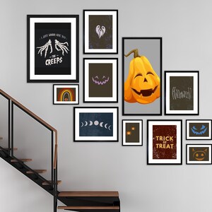 May include: A gallery wall of framed Halloween-themed art. The collection includes a pumpkin illustration, text that reads "Trick or Treat", and other spooky designs. The frames are black, and the art is displayed on a gray wall.