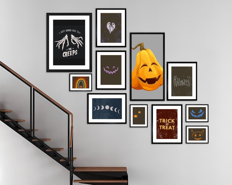 May include: A gallery wall of framed Halloween-themed art. The collection includes a pumpkin illustration, text that reads "Trick or Treat", and other spooky designs. The frames are black, and the art is displayed on a gray wall.
