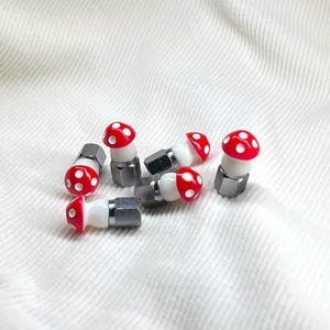 May include: A set of six red and white mushroom-shaped tire valve stem caps. The caps are made of plastic and have a silver metal base.