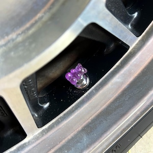 Könnte beinhalten: Eine Reifenventilkappe in Form eines lila Gummibärchens.