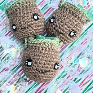 May include: Three crocheted brown ornaments with green tops and black eyes. The ornaments are on a striped red and green background with clear glass ornaments.