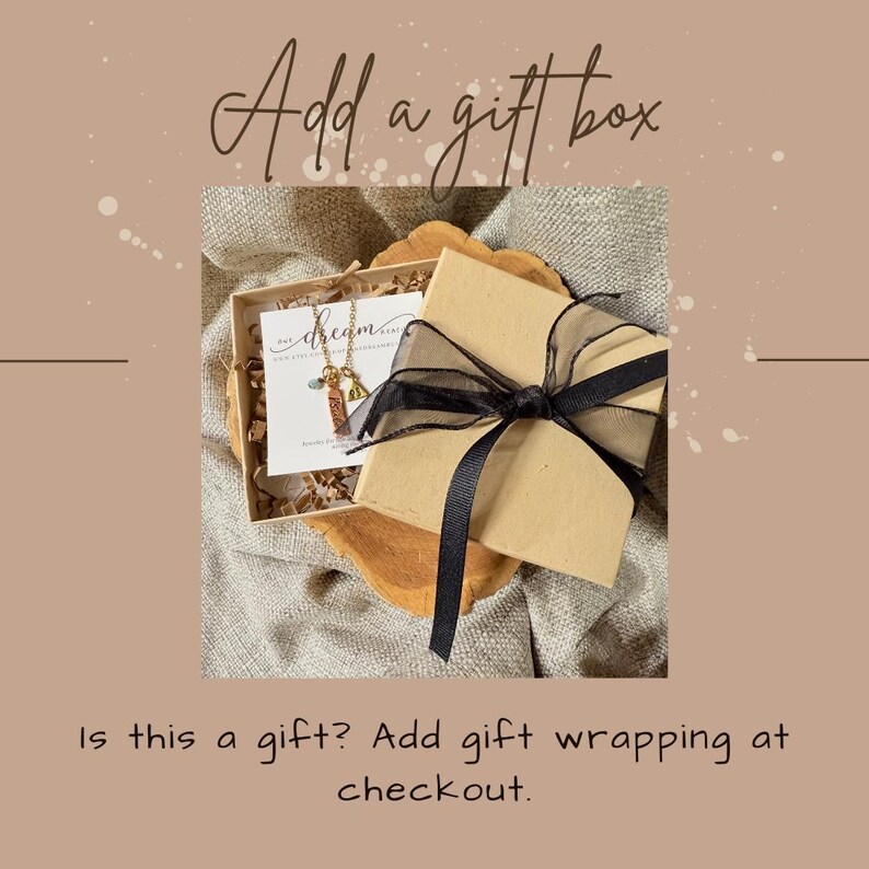 May include: A gift box tied with a black ribbon bow. Inside the box is a necklace and a card. The image text reads "Add a gift box" and "Is this a gift? Add gift wrapping at checkout."