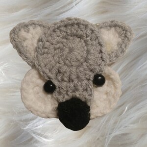 May include: A crocheted gray and white koala head with black eyes and a black nose.