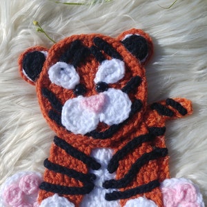 May include: A crocheted tiger toy with orange and black stripes, white accents, and pink paw pads.