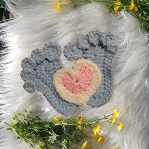 May include: Two crocheted baby booties in light blue with a pink and white heart applique on one bootie.