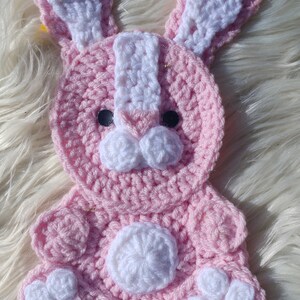 May include: A pink crocheted bunny with white accents. The bunny has a white nose, white ears, and white feet.