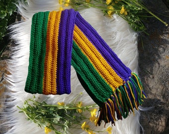 May include: A green, purple, and gold striped crocheted scarf with long fringe tassels. The scarf is made of yarn and has a soft, textured look.