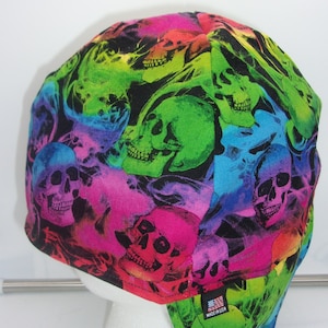 May include: A black welding cap with a colorful skull pattern. The skulls are in shades of pink, blue, green, and yellow. The cap has a flap in the back and a label that says "Made in USA".