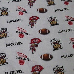 May include: A white fabric featuring a repeating pattern of Ohio State Buckeyes logos, brown footballs, red basketballs in hoops, and a mascot character holding an Ohio State flag. The text BUCKEYES and OHIO STATE is printed throughout the design.